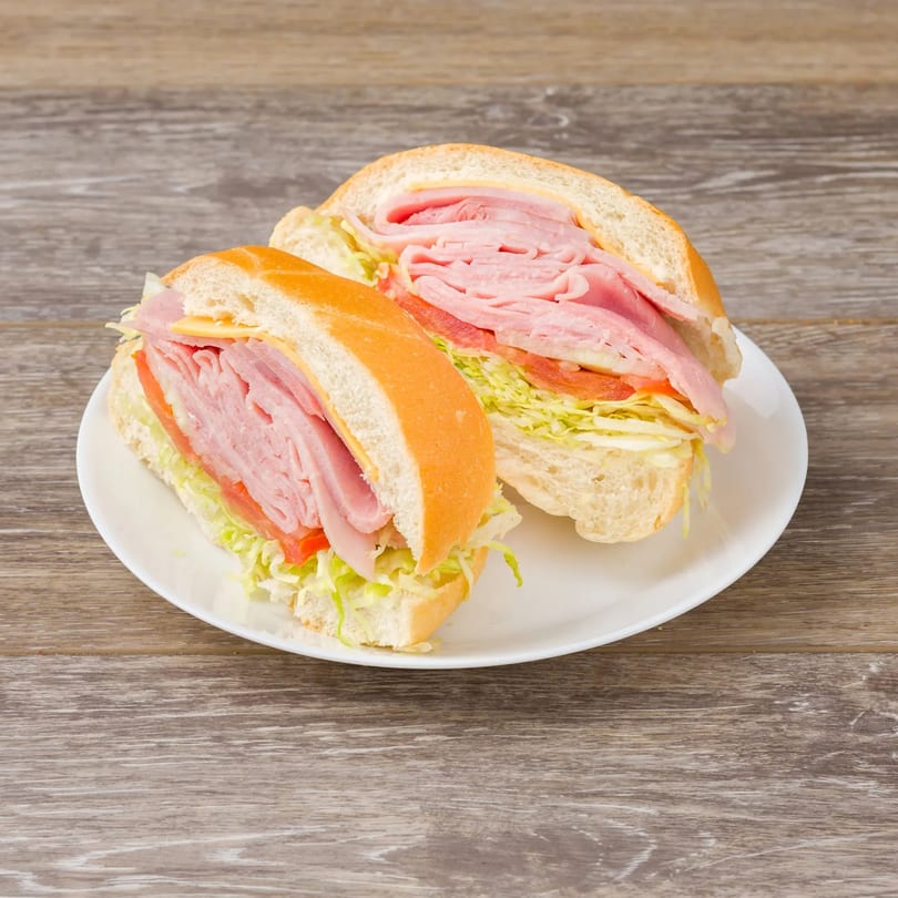 Two halves of a ham and cheese sub sandwich with lettuce and tomato on a white plate.