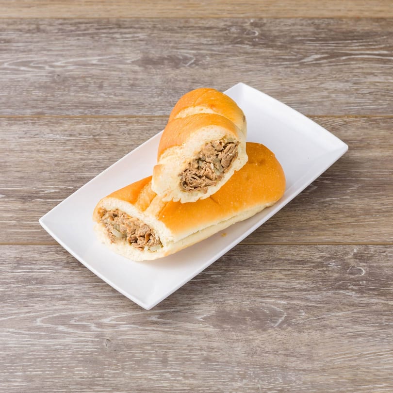 Two halves of a Philly cheesesteak sandwich with steak and onions on a white rectangular plate.