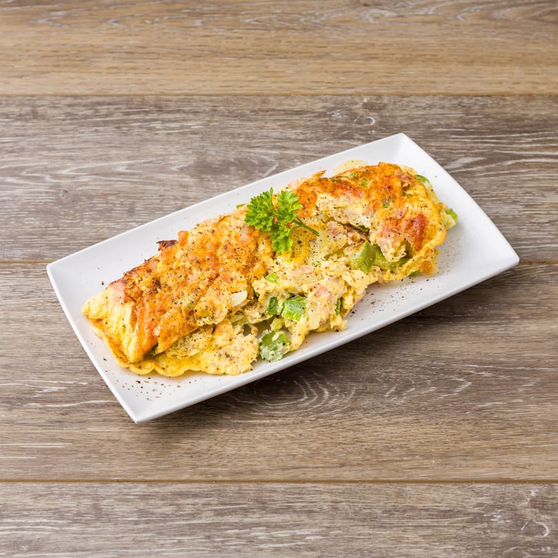 A golden-brown omelet filled with green peppers and cheese, garnished with parsley on a white plate.